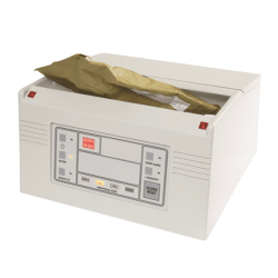 De afbeelding toont een röntgenapparaat met een open bovenpaneel. Binnenin is een bruin pakket zichtbaar. Het apparaat heeft knoppen en indicatoren op de voorkant.